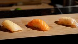 Three pieces of nigiri sushi placed in a row on a wooden board, featuring different types of fish with a blurred background.