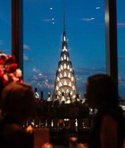 Night view of the illuminated Chrysler Building from a high-rise event space with silhouetted guests and a bar setup