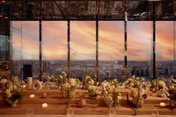 Event space with panoramic city views through floor-to-ceiling windows at sunset, decorated with floral arrangements.