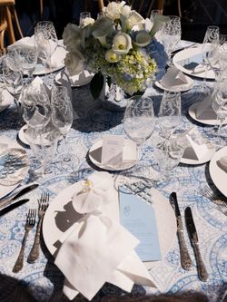 Table set for a wedding with white floral centerpiece, glassware, utensils, and blue patterned tablecloth at Midtown event.