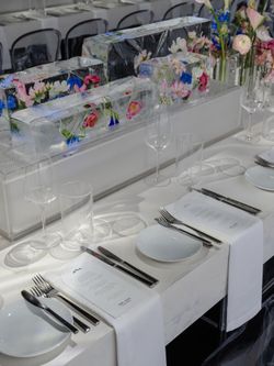 Elegant table setting with white napkins, cutlery, menus, and decorative ice blocks with flowers inside at an event space.