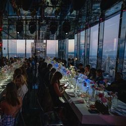 Midtown event space in NYC with glass walls offering panoramic city views, set for a formal dinner event with floral center