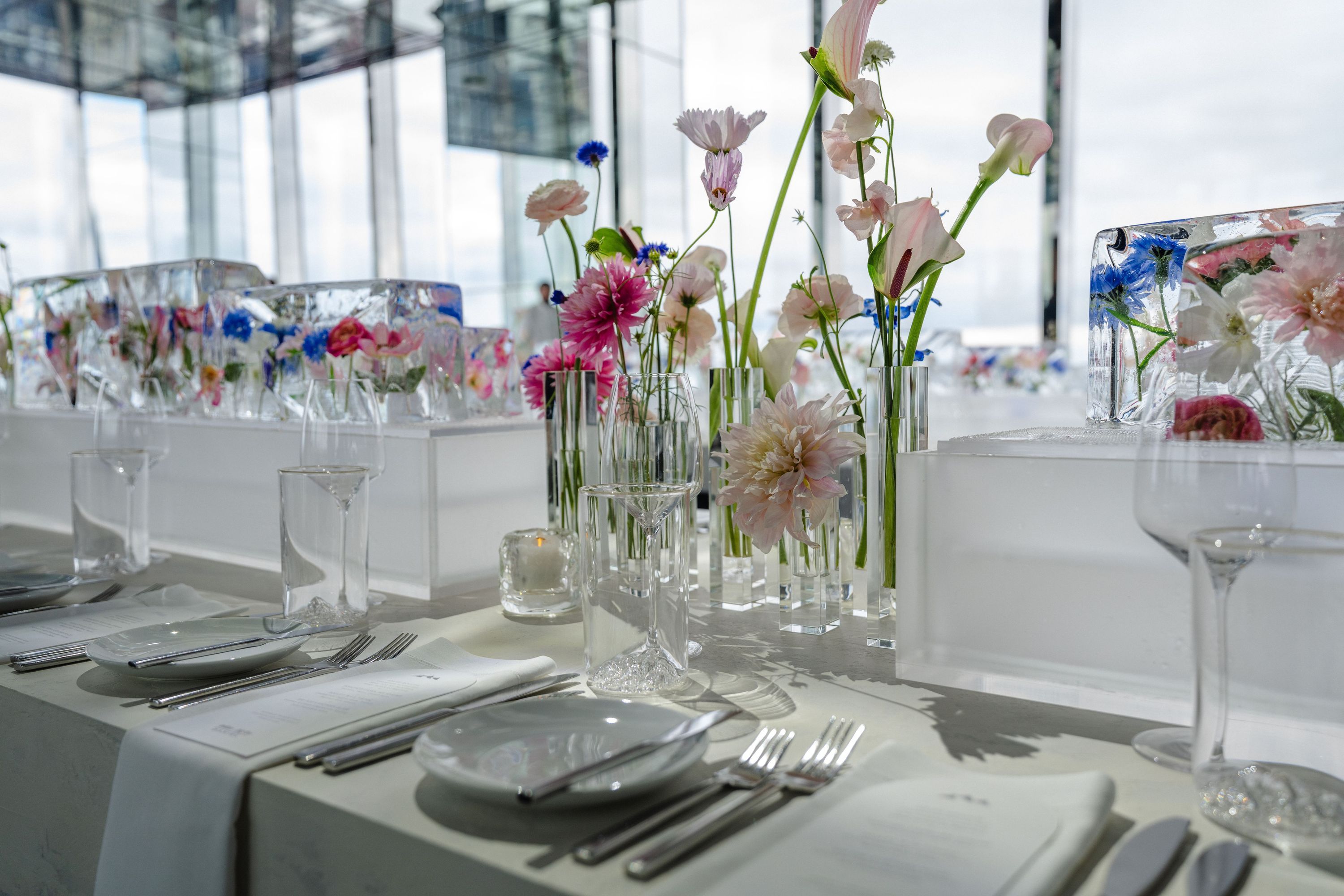 Elegant dining setup featuring floral centerpieces in a modern event space with city views.